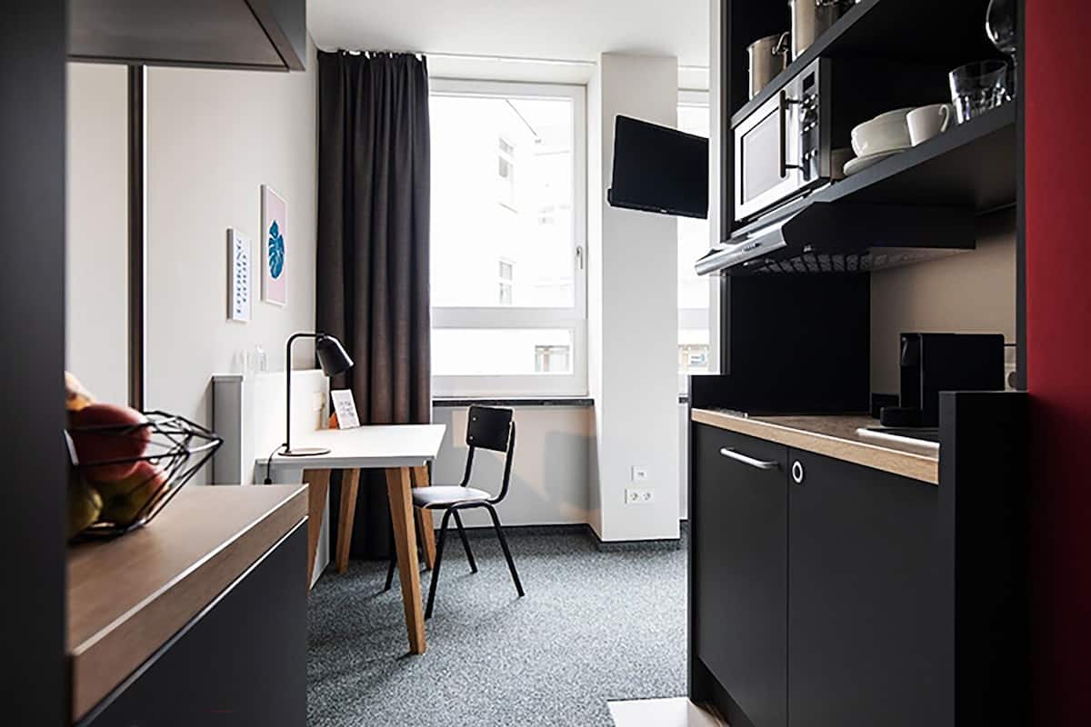 A compact kitchen with a dining area, a window with curtains, and a flat-screen TV mounted above the counter.