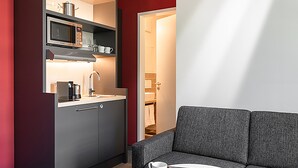 Une cuisine moderne équipée d’un four à micro-ondes, d’une machine à café et de placards. On y trouve un canapé gris et une petite table avec une tasse blanche.