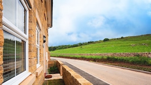 A stone building with large windows and a paved road leading to a green field. - Peak District New Modern Cottage in Buxton (Buxton)