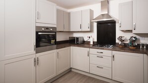 A modern kitchen with white cabinets, stainless steel appliances, and a wooden countertop. - Peak District New Modern Cottage in Buxton (Buxton)