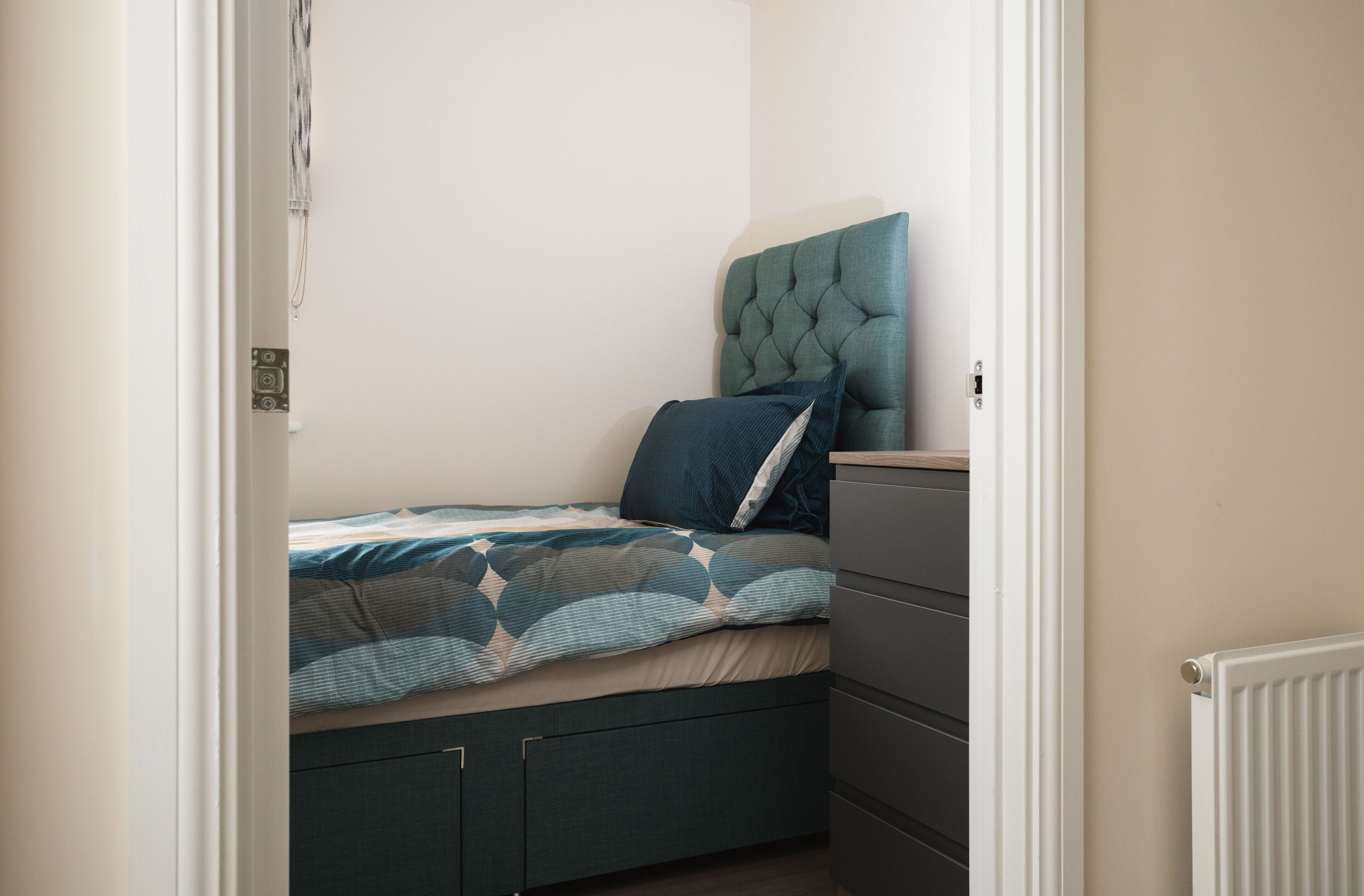 A bedroom with a bed, a dresser, and a radiator.