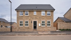 A two-story stone house with a black roof, a front door, and multiple windows. - Peak District New Modern Cottage in Buxton (Buxton)