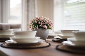 A dining table with white plates and a central vase with pink flowers. - Peak District New Modern Cottage in Buxton (Buxton)
