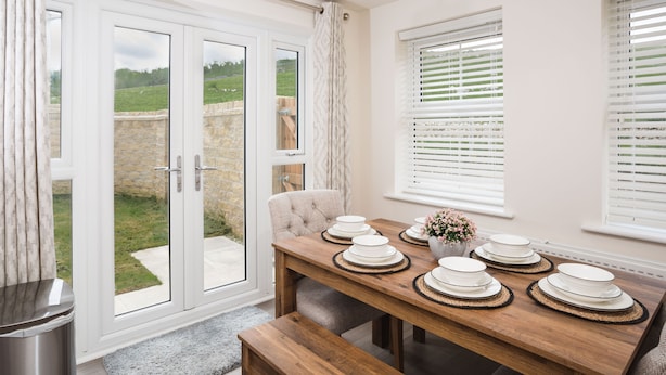 A dining area with a wooden table set for four, a bench, and a view through glass doors to a garden. - Peak District New Modern Cottage in Buxton (Buxton)