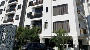 Un immeuble résidentiel à plusieurs étages, doté de balcons, avec un panneau indiquant la limite de vitesse et une zone de stationnement où se trouve une voiture noire.