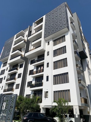 A multi-story residential building with balconies, a speed limit sign, and a parking area with a black car.
