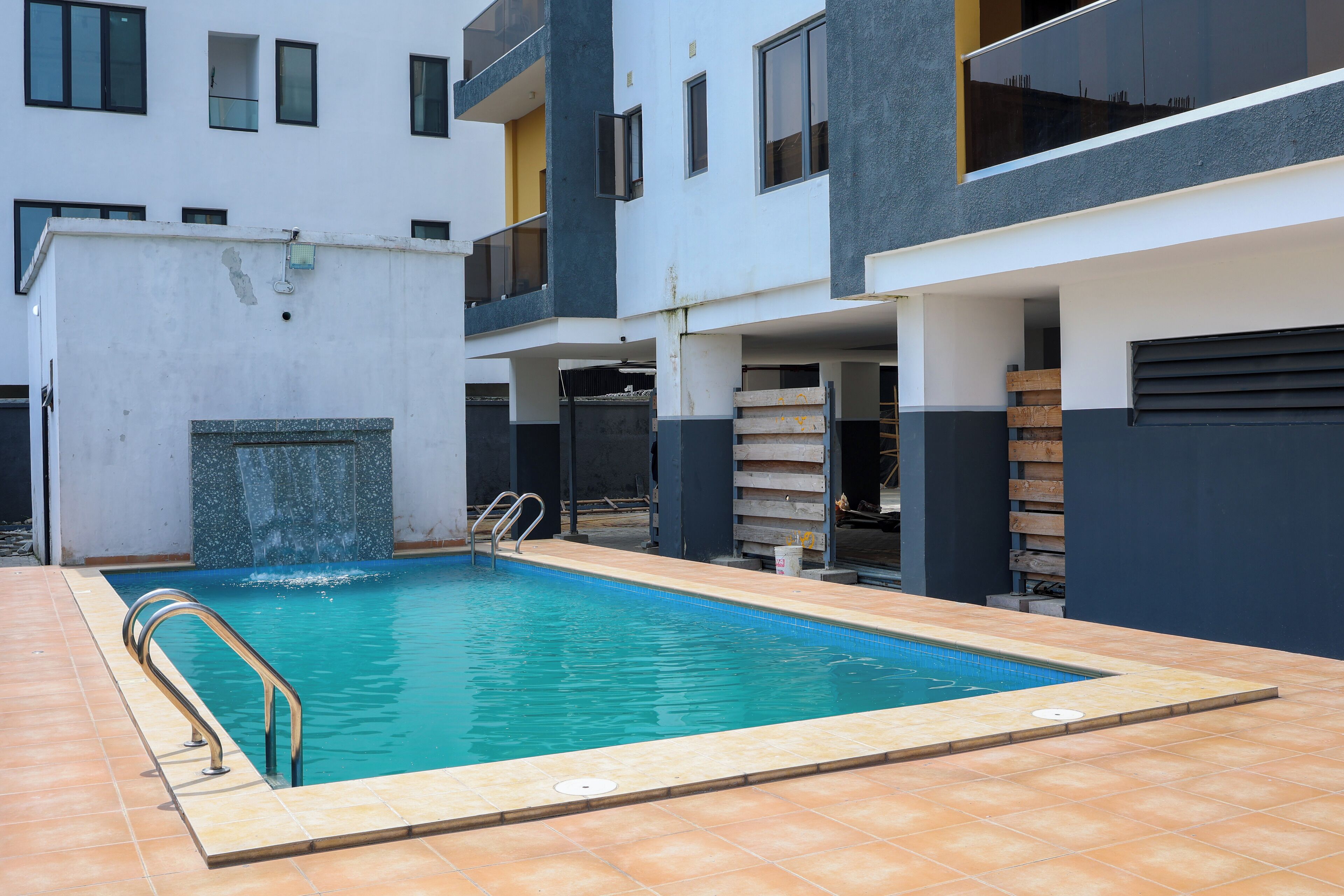 A swimming pool with a metal handrail, surrounded by a tiled patio.