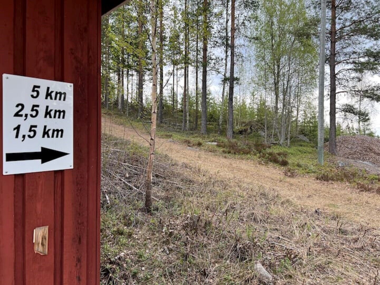 A sign with distance markers (5 km, 2.5 km, 1.5 km) and an arrow pointing right, indicating a trail or path in a forested area.