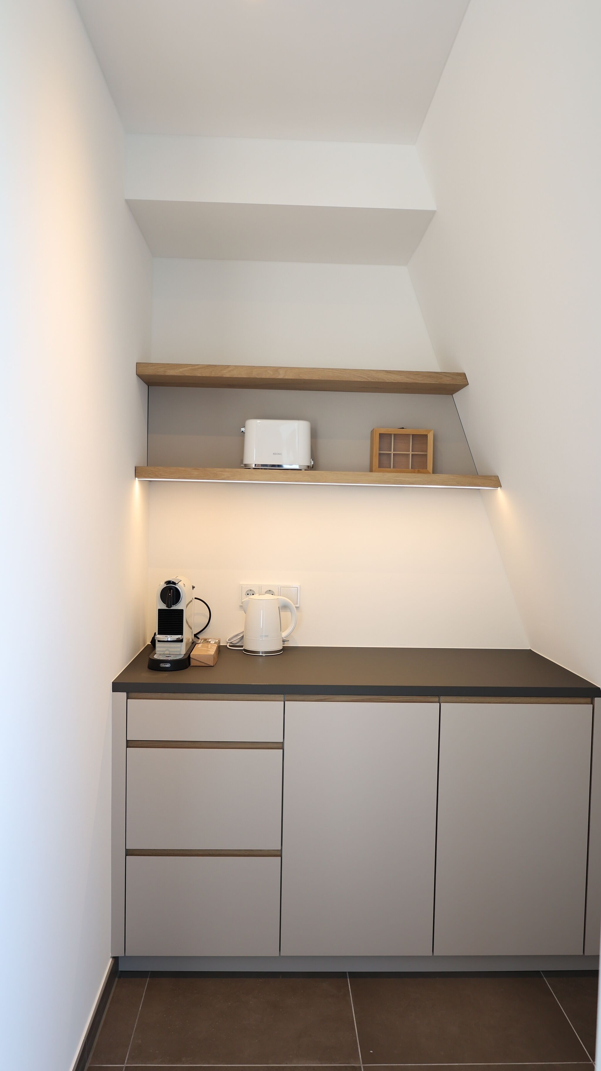 Une cuisine compacte équipée d’un plan de travail, d’une machine à café, d’une bouilloire et d’une étagère au-dessus.