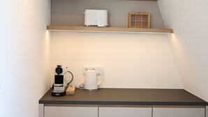 Cocina compacta con mostrador, cafetera, hervidor y estante superior.
