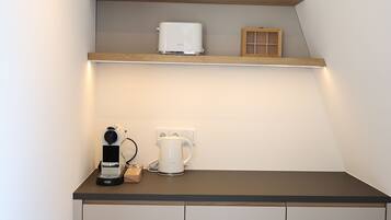 Une cuisine compacte équipée d’un plan de travail, d’une machine à café, d’une bouilloire et d’une étagère au-dessus.