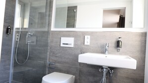 Un baño moderno con ducha de vidrio, lavamanos blanco y retrete.