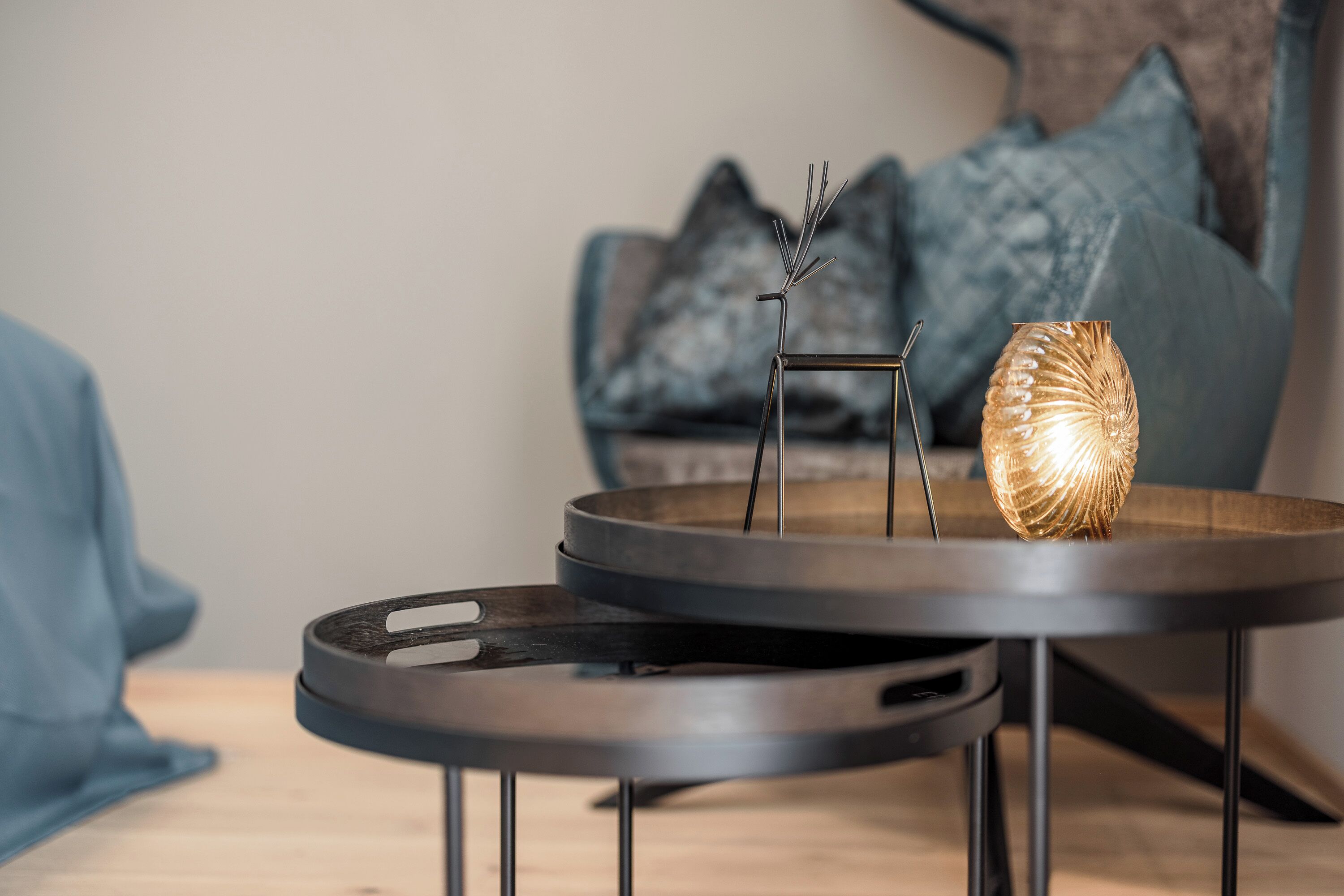 A modern living room with two round tables, one with a candle holder and a decorative metal piece.