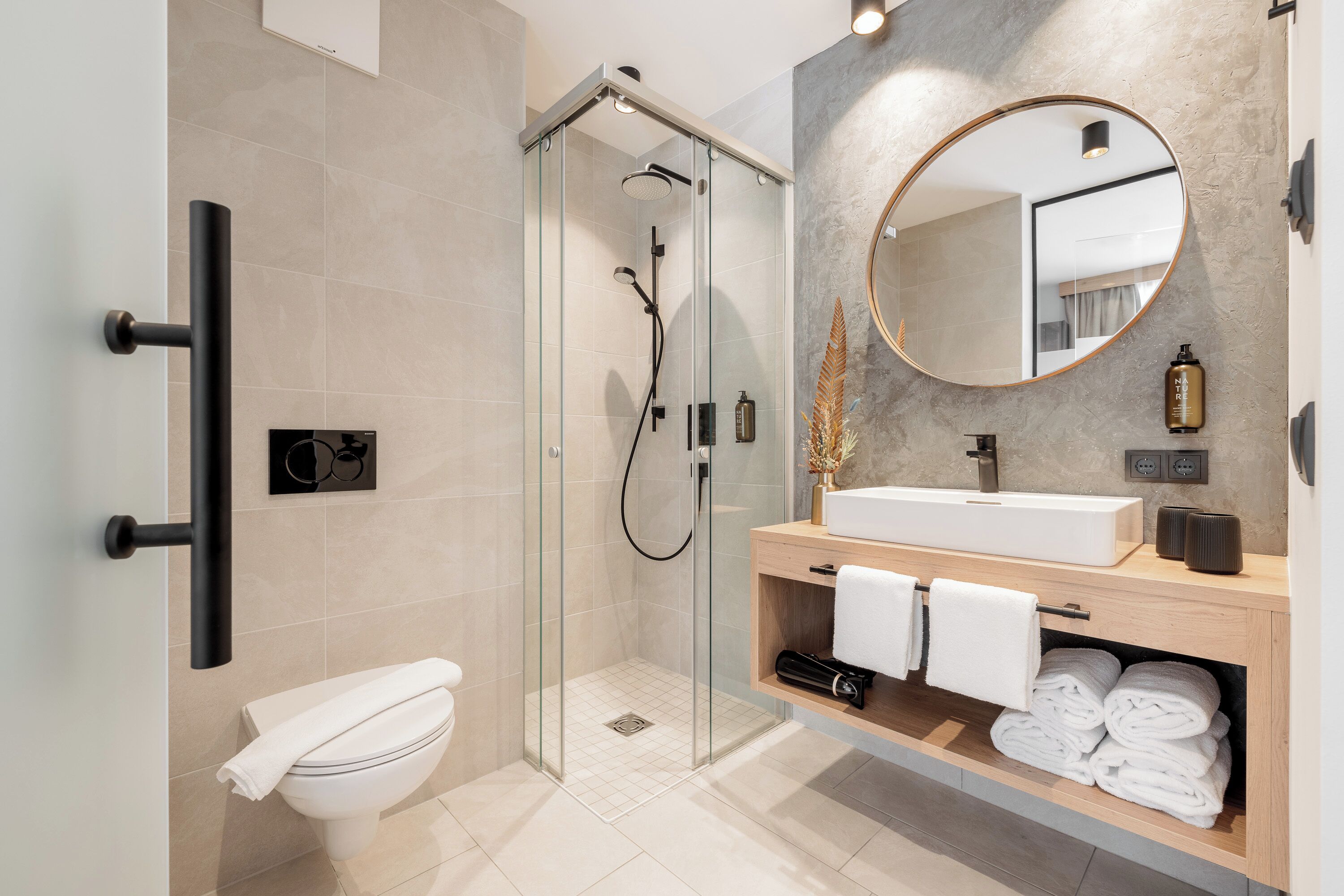 A modern bathroom with a glass-enclosed shower, a white toilet, a wooden vanity with a large mirror, and neatly folded towels.