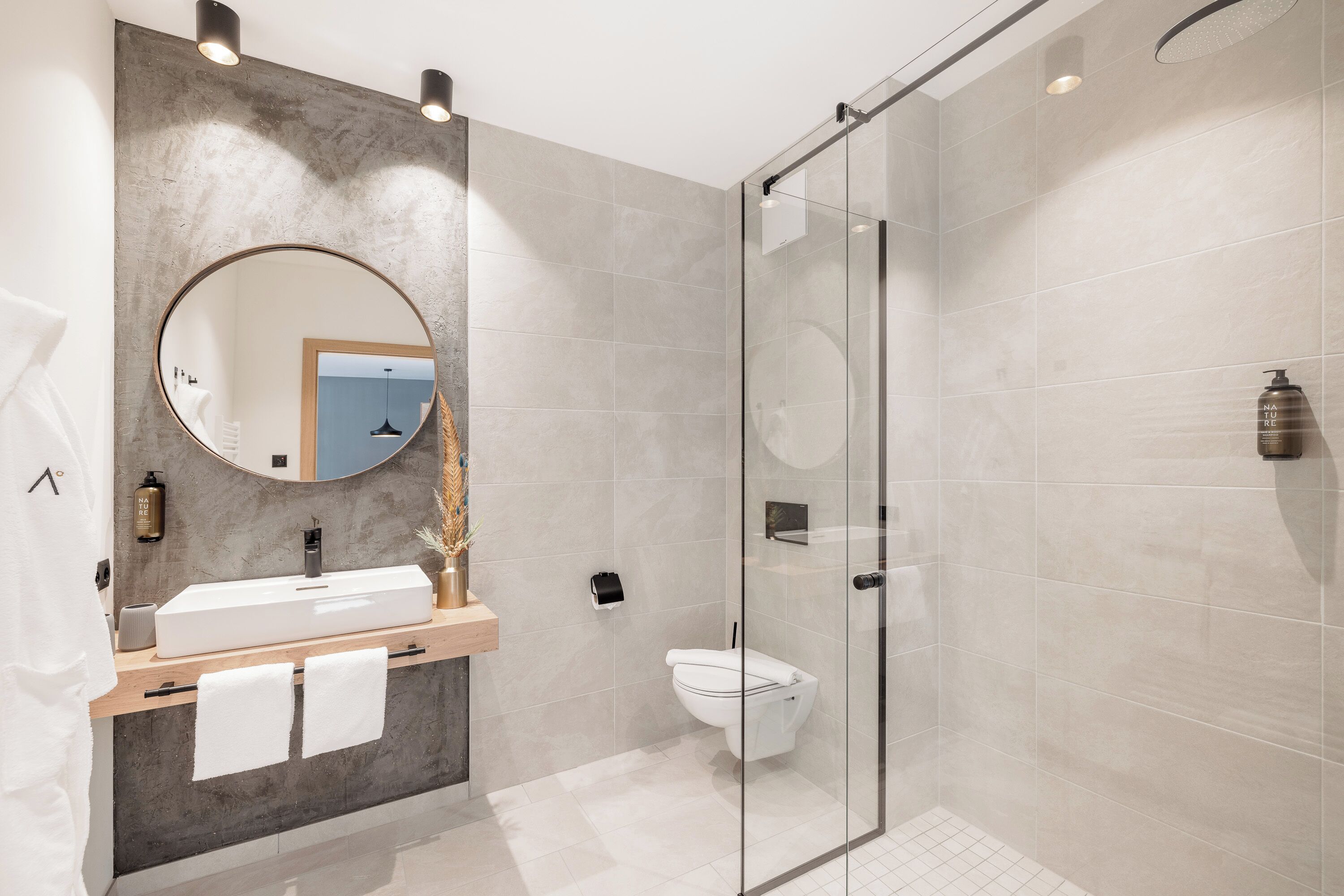 Et moderne badeværelse med et glasvæg-afskærmet brusebad, et rundt spejl og en trækommode.