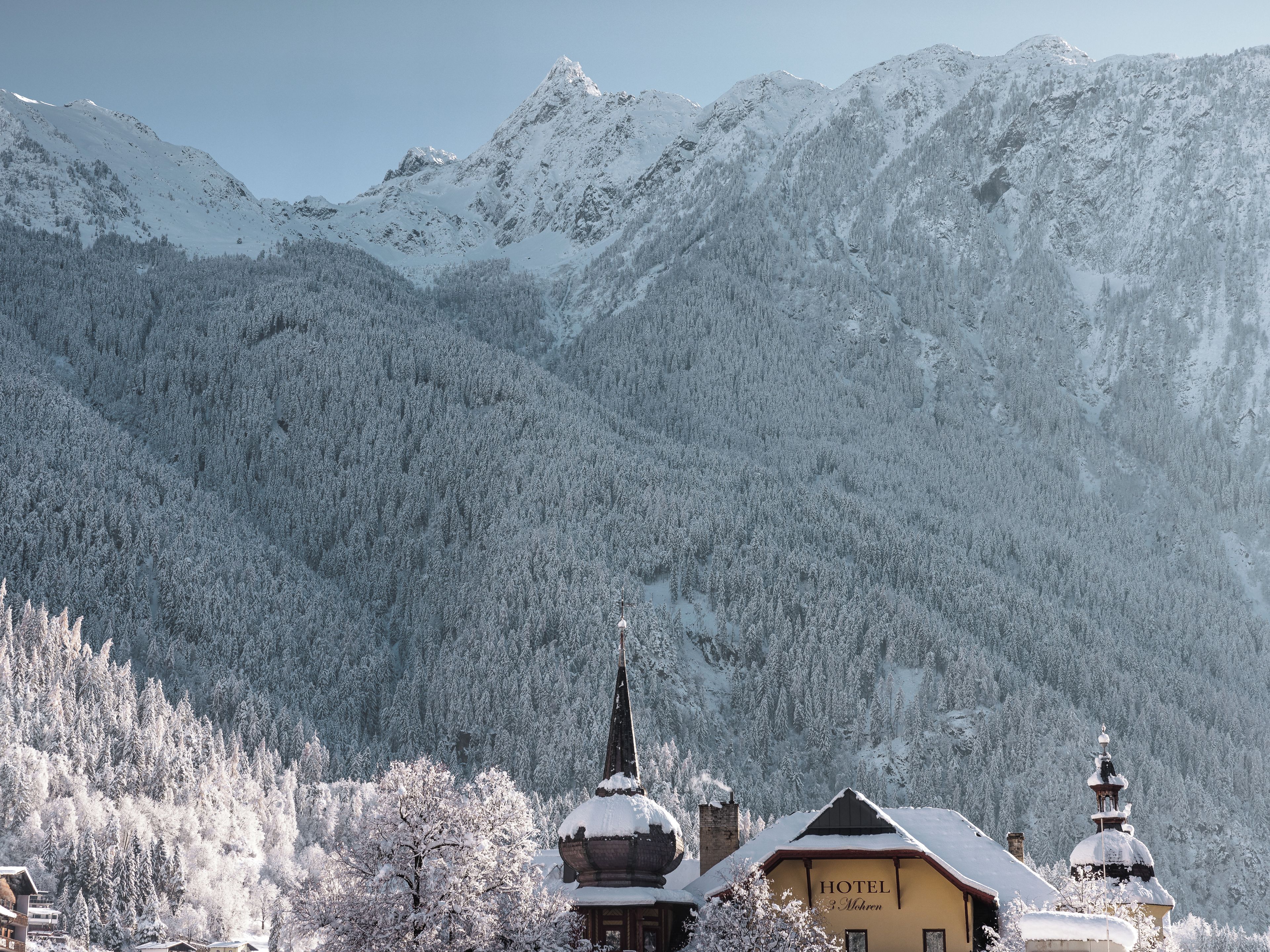 Ein Hotel vor einer schneebedeckten Berglandschaft, mit einem markanten Kirchturm und einem Gebäude mit Kuppel.