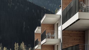 Ein modernes, mehrstöckiges Gebäude mit Balkonen, Holzverkleidung und einem Bergpanorama.