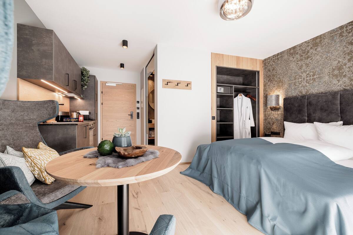 Habitació d'hotel moderna amb un llit, una taula rodona, un sofà i una cuineta.
