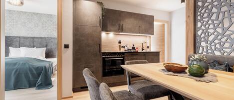 A modern kitchen with dark cabinets, a wooden dining table, and a grey upholstered bench.