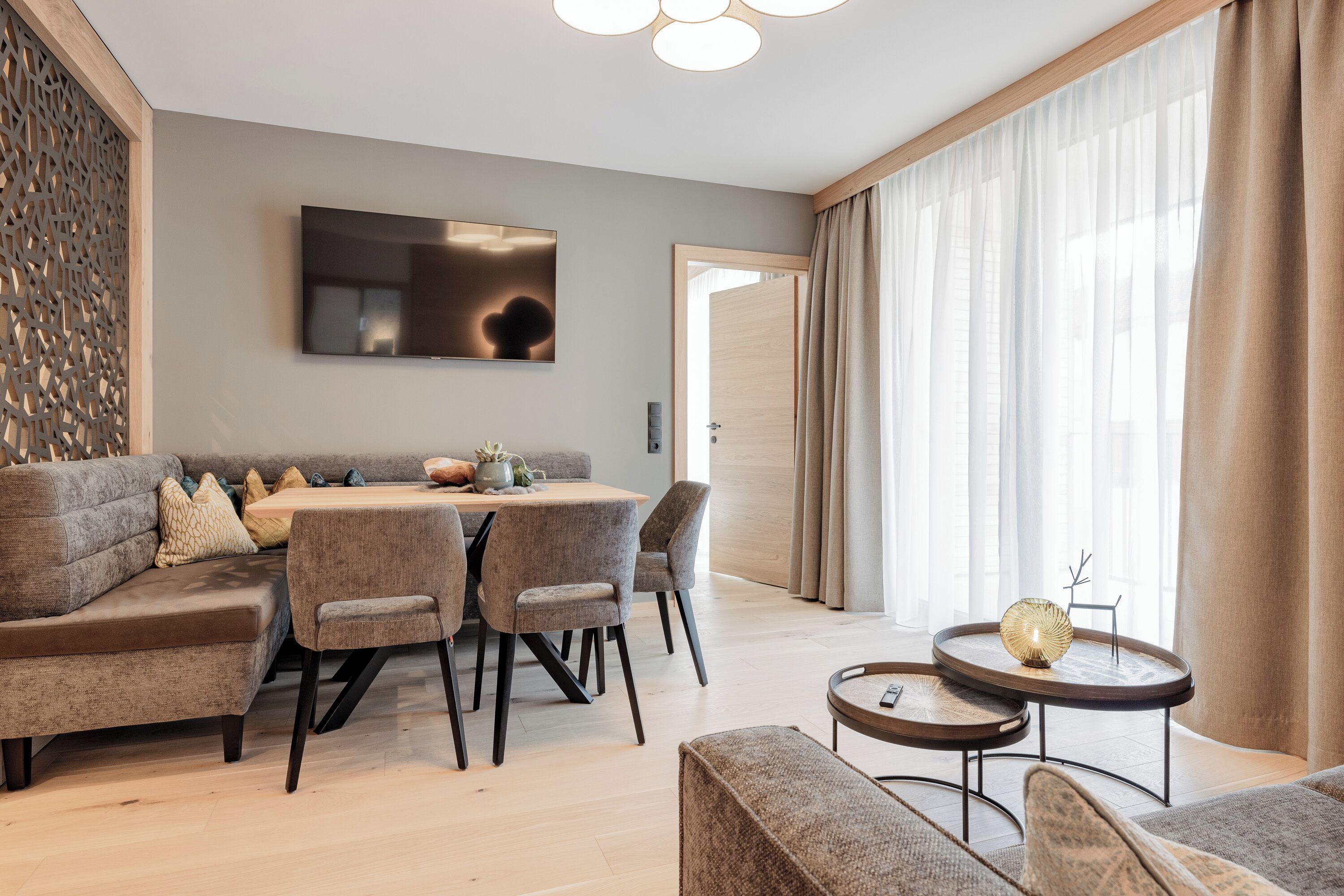 A modern living room with a sofa set, a dining table, and a TV mounted on the wall.