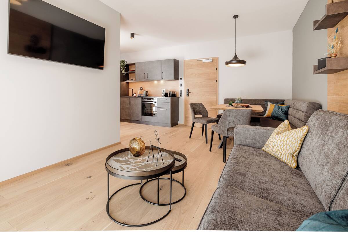Un saló modern amb un sofà gris, una taula de centre rodona i una zona de menjador amb taula i cadires de fusta.