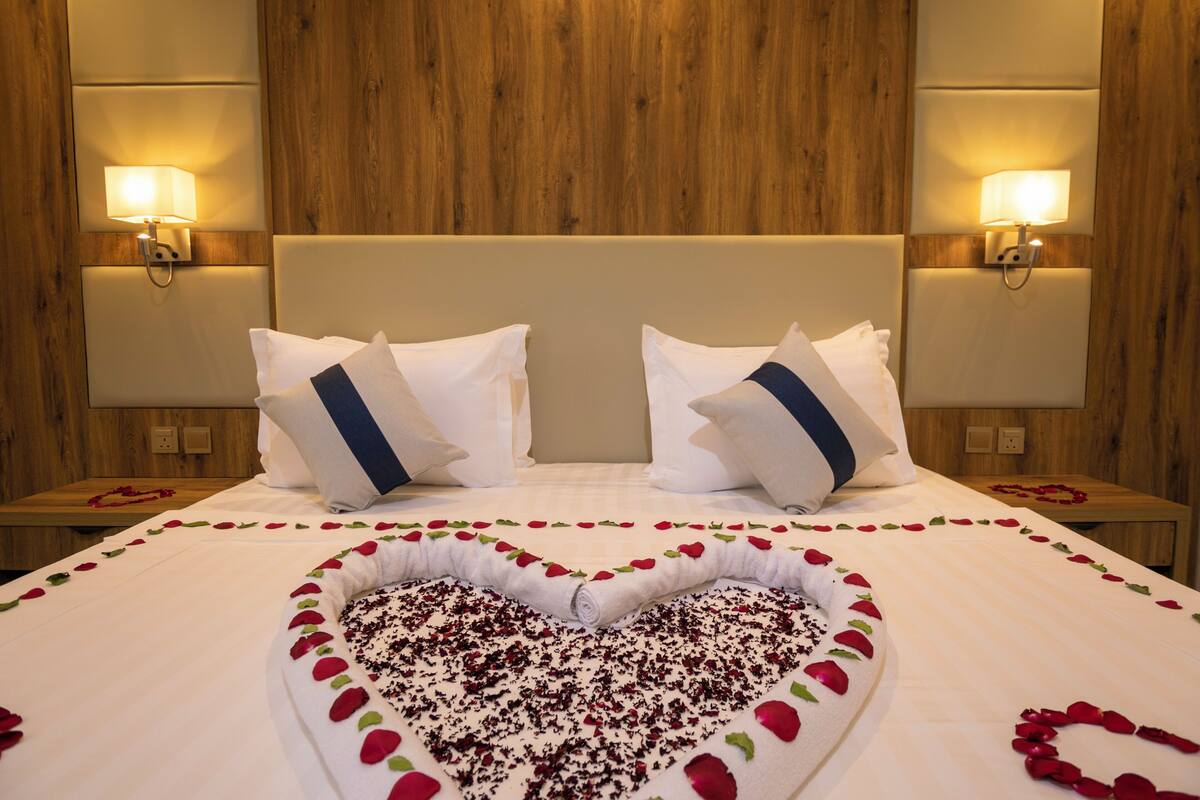 A hotel room with a large bed, two nightstands, and wall-mounted lamps.