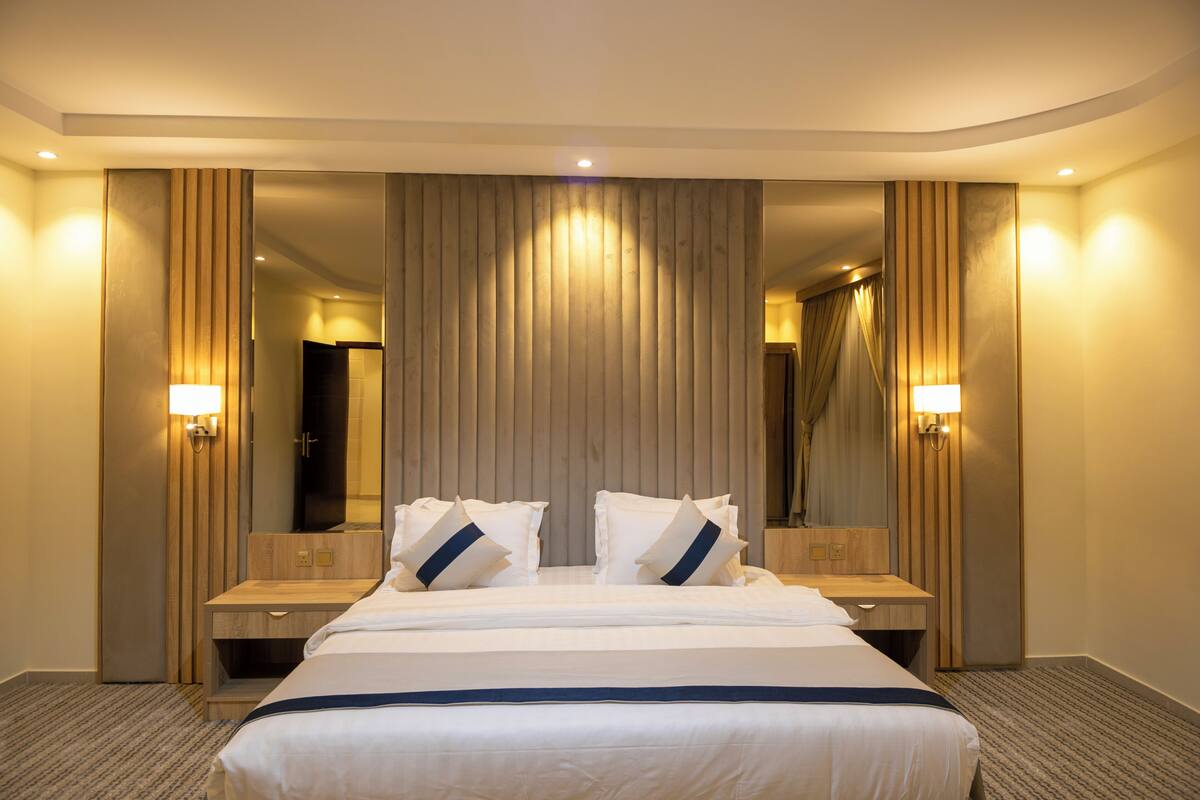 A hotel room with a large bed, two bedside tables, a mirror, and wall-mounted lamps.