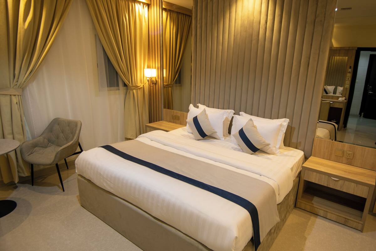 A hotel room with a large bed, a chair, a nightstand, and a mirror.