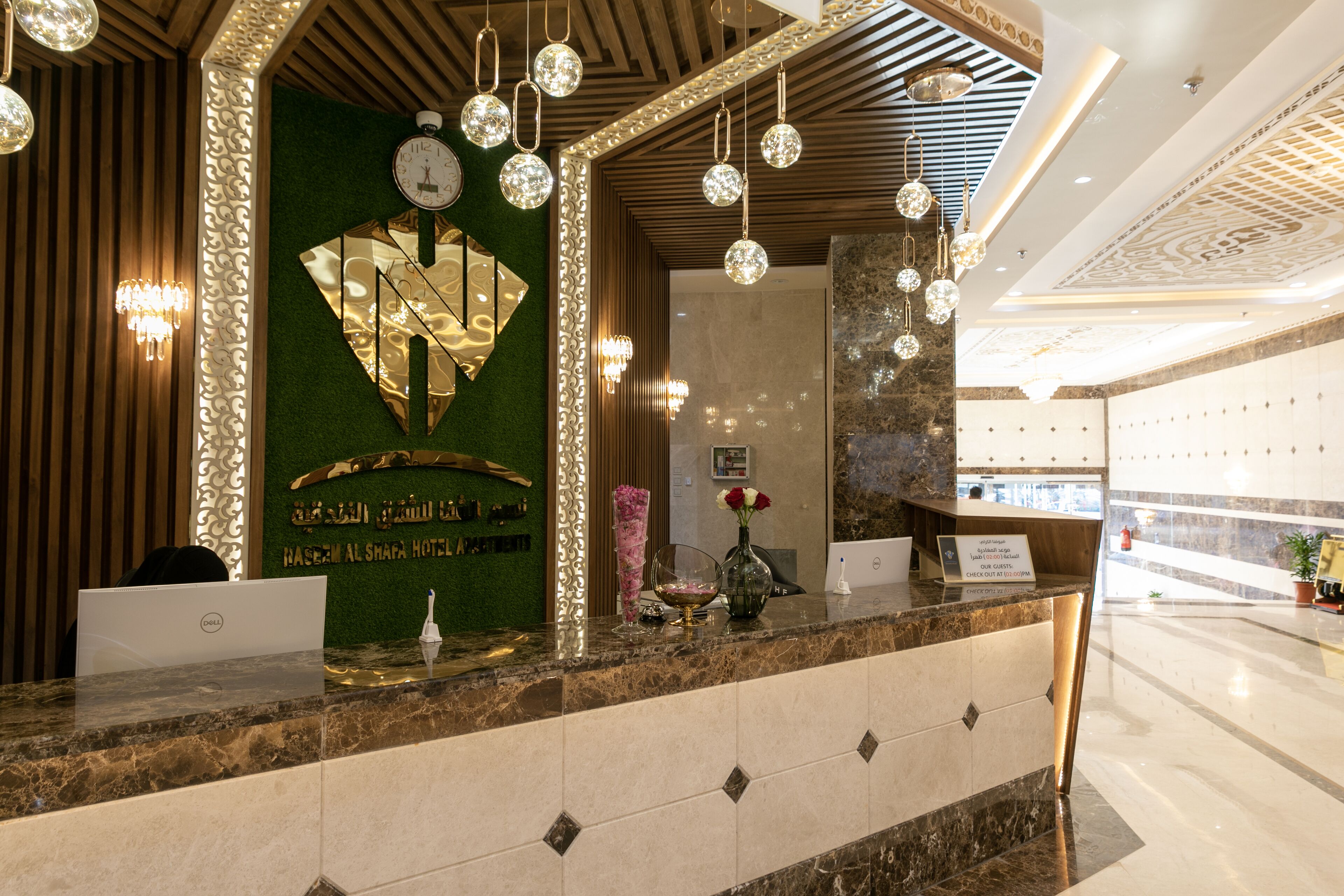 Un espace d’accueil d’hôtel avec un comptoir en marbre, une horloge et un mur décoratif sur fond vert.