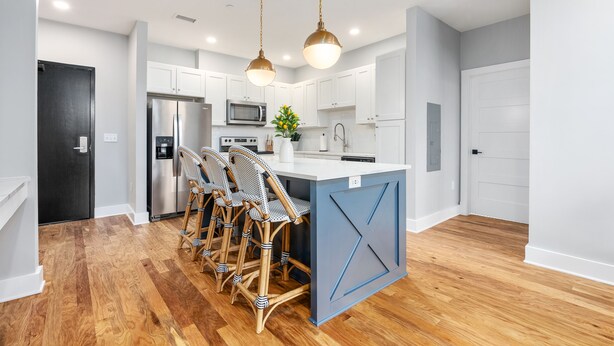 A modern kitchen with a central island, wooden flooring, white cabinetry, and hanging pendant lights. - Lavish Apartment over Target in Downtown Auburn - 205 (Auburn)