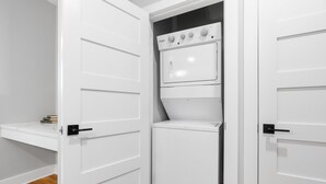 A laundry room with a front-loading washer and dryer, a small shelf with books, and a wooden floor. - Lavish Apartment over Target in Downtown Auburn - 205 (Auburn)