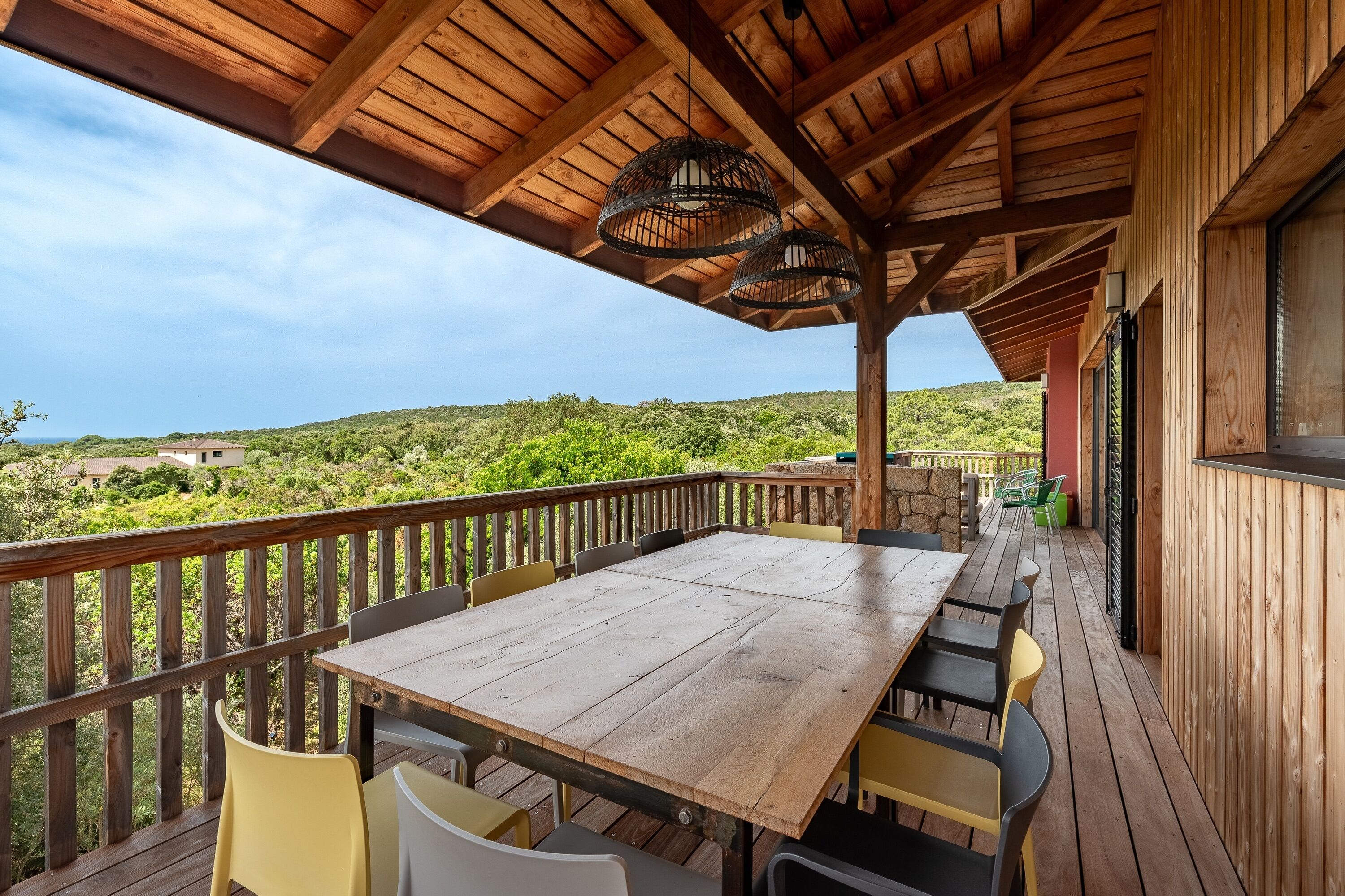 Una terraza de madera con una mesa y sillas, con vistas a un paisaje exuberante.