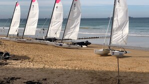 A row of sailboats with numbered sails lined up on a sandy beach.