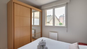 A bedroom with a bed, a wooden wardrobe, a window with a view of buildings, and a radiator.