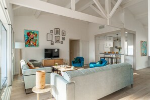 Un salon spacieux avec un grand canapé, un téléviseur et un coin repas à l’arrière-plan.
