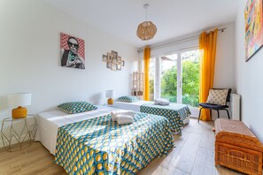 Une chambre avec deux lits, une fenêtre avec des rideaux, une petite table et une chaise.
