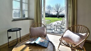 Ein Zimmer mit zwei Korbstühlen, einem kleinen Tisch und einem Fenster mit Jalousien.
