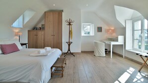 Ein Schlafzimmer mit einem Bett, einem Holzschrank, einem Schreibtisch, einem Stuhl, einer Stehlampe und einem Fenster.