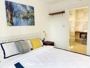 Un dormitorio con cama, mesita de noche, un cuadro y baño completo con ducha e inodoro.