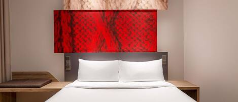 Una habitación de hotel moderna con una cama grande, una mesita de noche de madera y un cabecero con controles integrados.