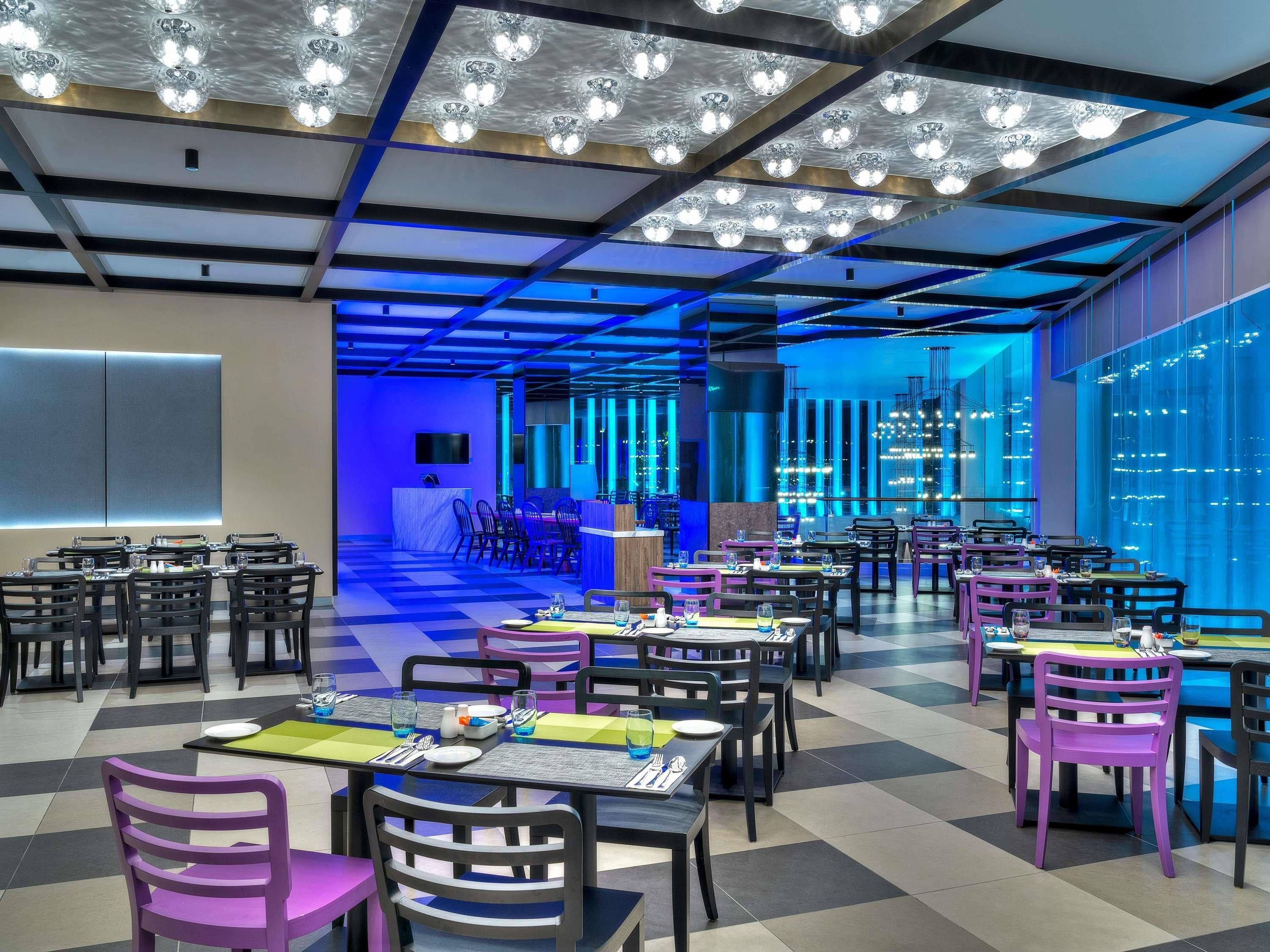 Een modern restaurant met een zwart-witte vloer, tafels met stoelen en een blauw verlicht plafond.