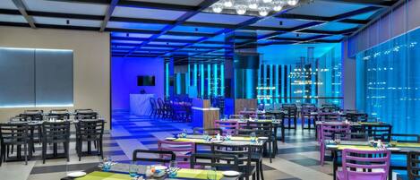 Een modern restaurant met een zwart-witte vloer, tafels met stoelen en een blauw verlicht plafond.
