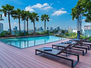 Une piscine sur le toit, avec des chaises longues, des palmiers et une vue imprenable sur le paysage urbain.