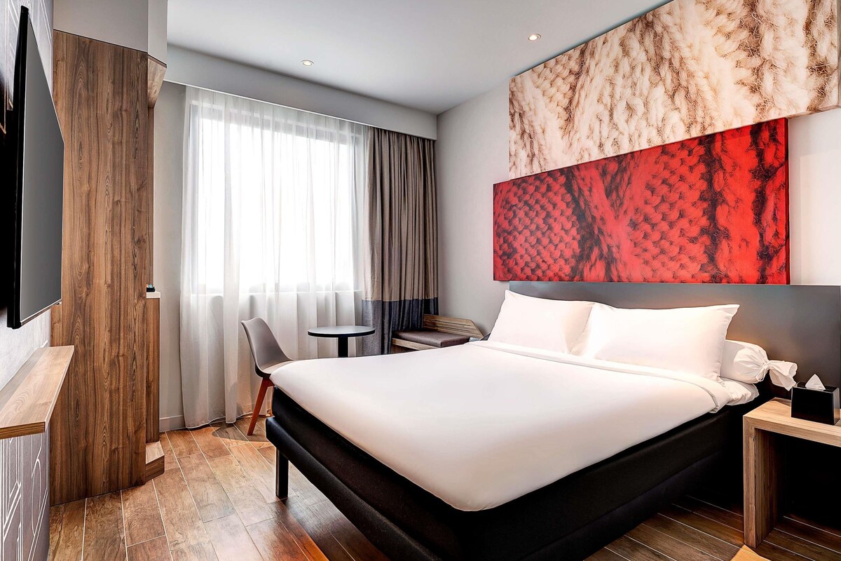 Ein modernes Hotelzimmer mit einem großen Bett, einem kleinen Tisch, einem Stuhl und einem Fernseher.
