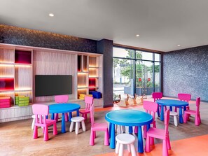 Un intérieur moderne avec un grand téléviseur, des chaises colorées et des tables disposées pour les repas ou les réunions.