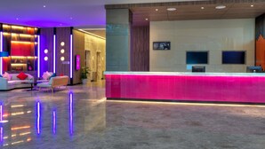 Een moderne hotel lobby met een receptiebalie, een zithoek en een groot scherm.