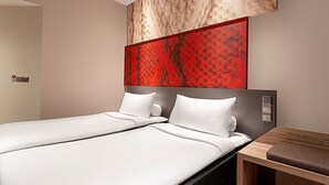 Een moderne hotelkamer met twee bedden, een houten nachtkastje en een abstract kunstwerk op de muur in rood.