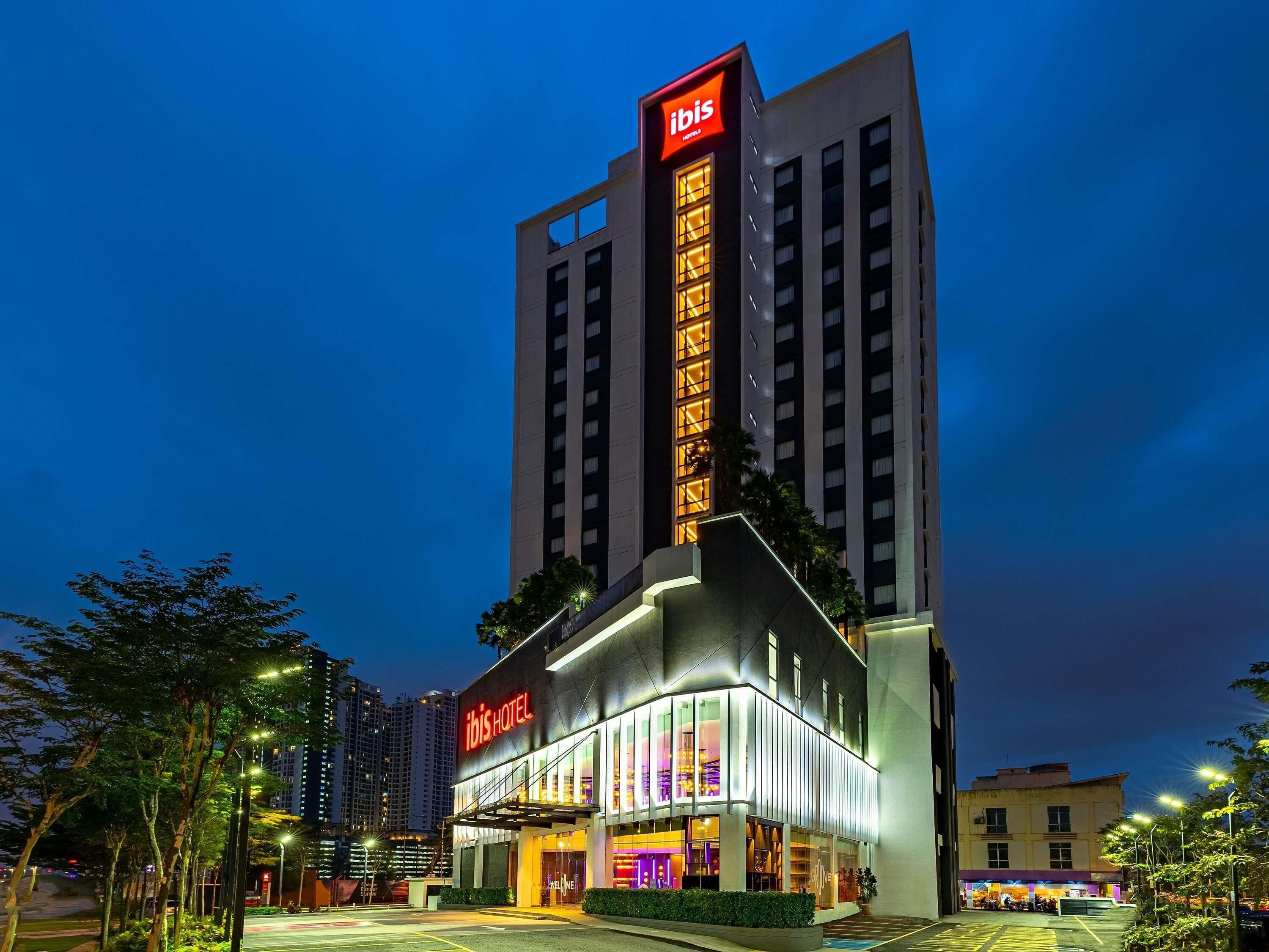 A modern hotel with a prominent 'ibis' sign, large windows, and a well-lit entrance.