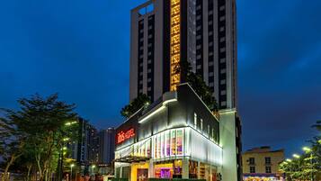 A modern hotel with a prominent 'ibis' sign, large windows, and a well-lit entrance.