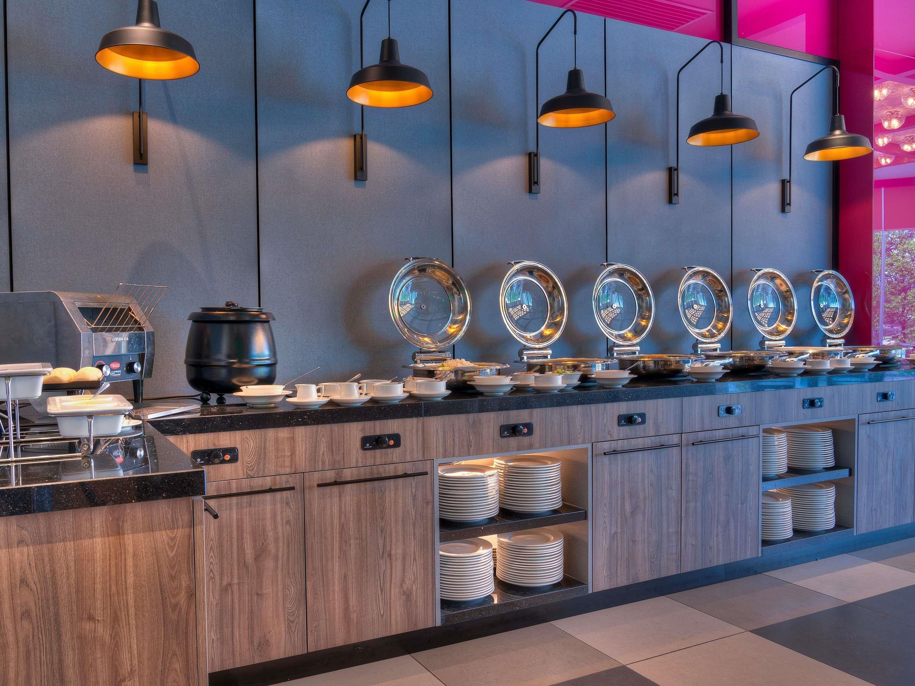 A modern kitchen with a coffee station, multiple light fixtures, and a counter with stacked plates.